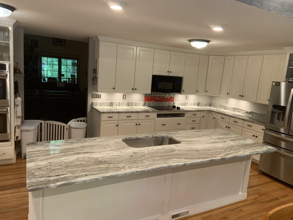 large over size kitchen island with natural granite countertop install
large walk in kitchen
white walls
light fixtures
stainless steel refrigerator
large kitchen 
large kitchen island with Brown Fantasy Granite 